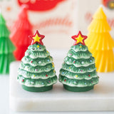 Two Christmas tree-shaped candles with star toppers on a white surface.